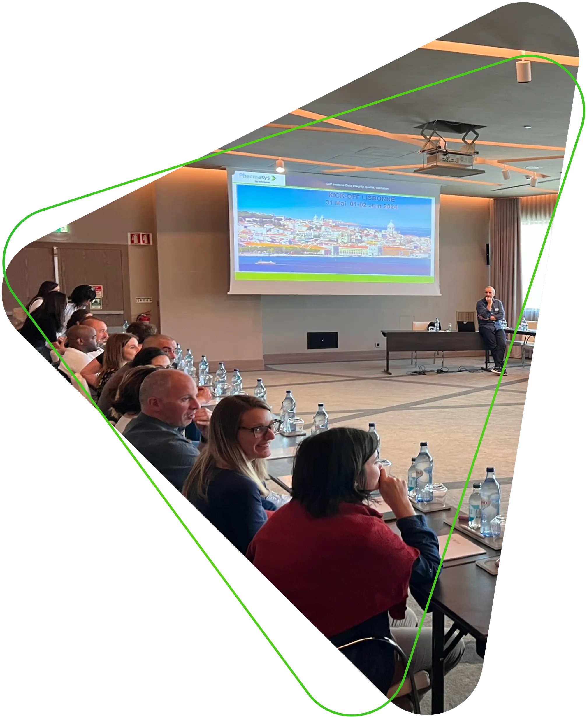 Un homme debout présente un graphique sur un écran à cinq collègues assis autour d’une table de réunion, dans une salle de conférence moderne. Tous portent des vêtements professionnels. L’image est encadrée par une forme triangulaire aux bords arrondis et soulignée par un trait vert dynamique.