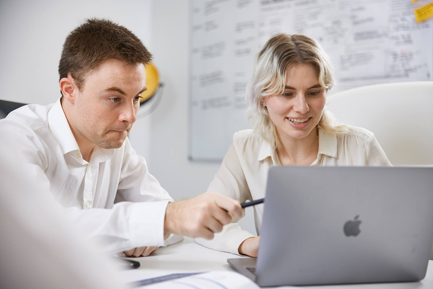 Two young professionals collaborating and pointing at a laptop screen in a modern office.