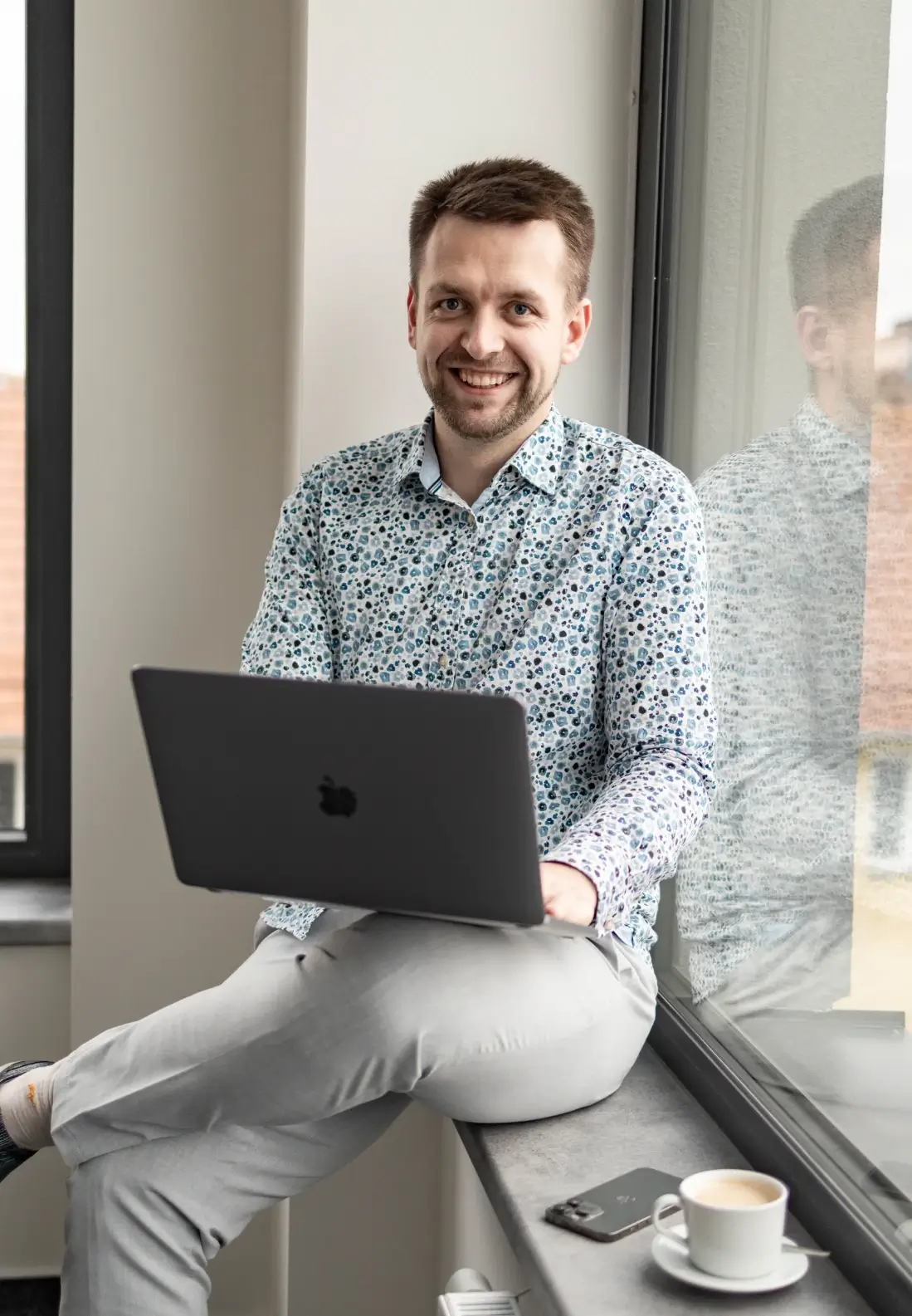 Zdenek Lehký, sedící na parapetu okna s macbookem. 