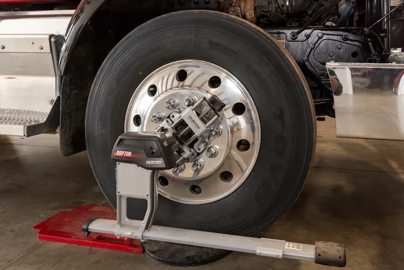 Wheel alignment with a heavy-duty truck connected to alignment equipment for steering and suspension adjustment.