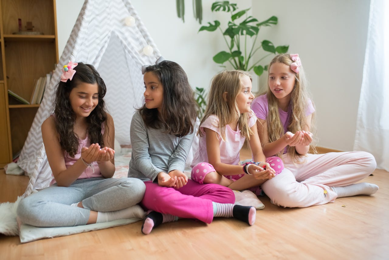 Four girls enjoying a cozy pajama party indoors, seated in a tent, sharing laughter and friendship