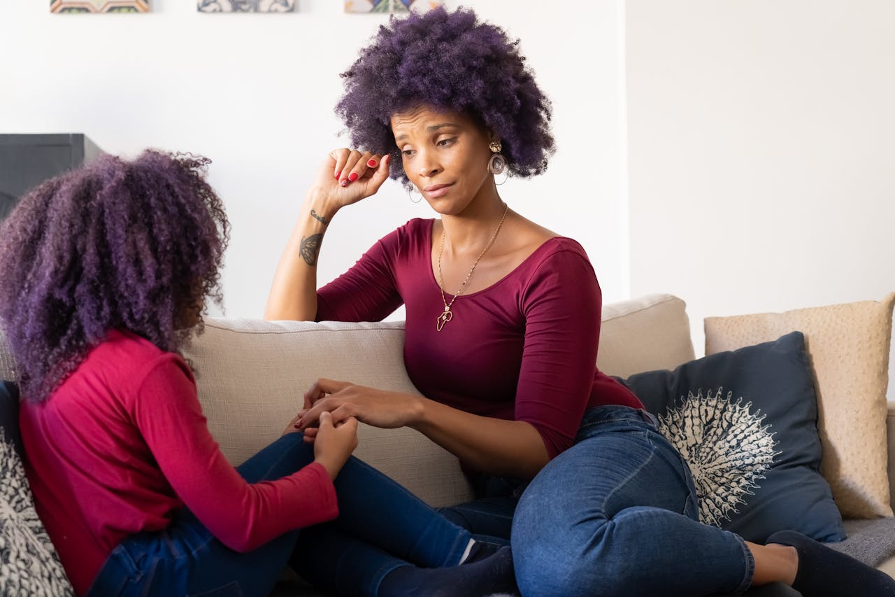 Mother and daughter with purple hair holding hands on the couch, sharing a moment of bonding and connection