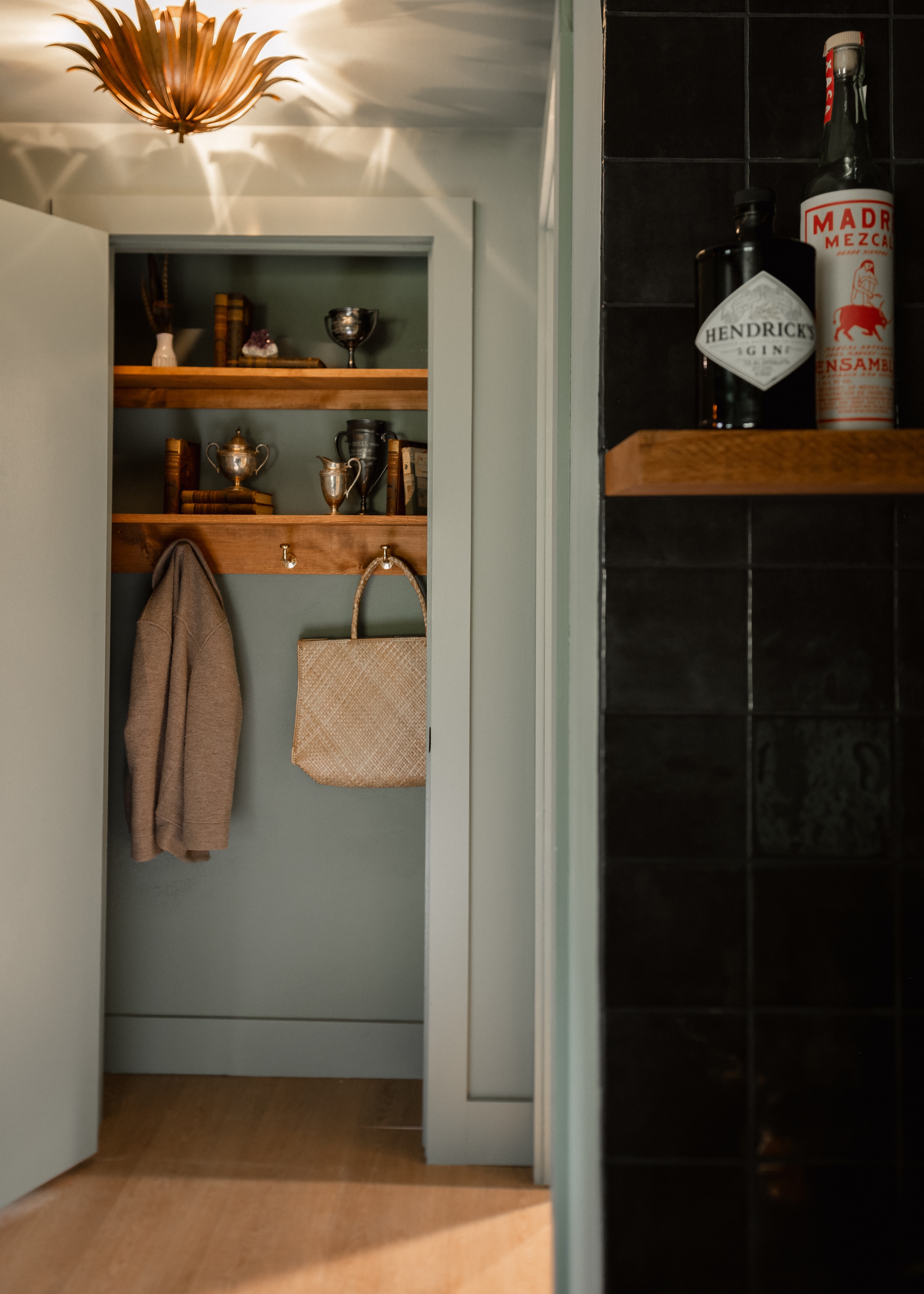 Open closet door revealing wooden shelves with trophies and books, a hanging tan jacket, and a woven bag.