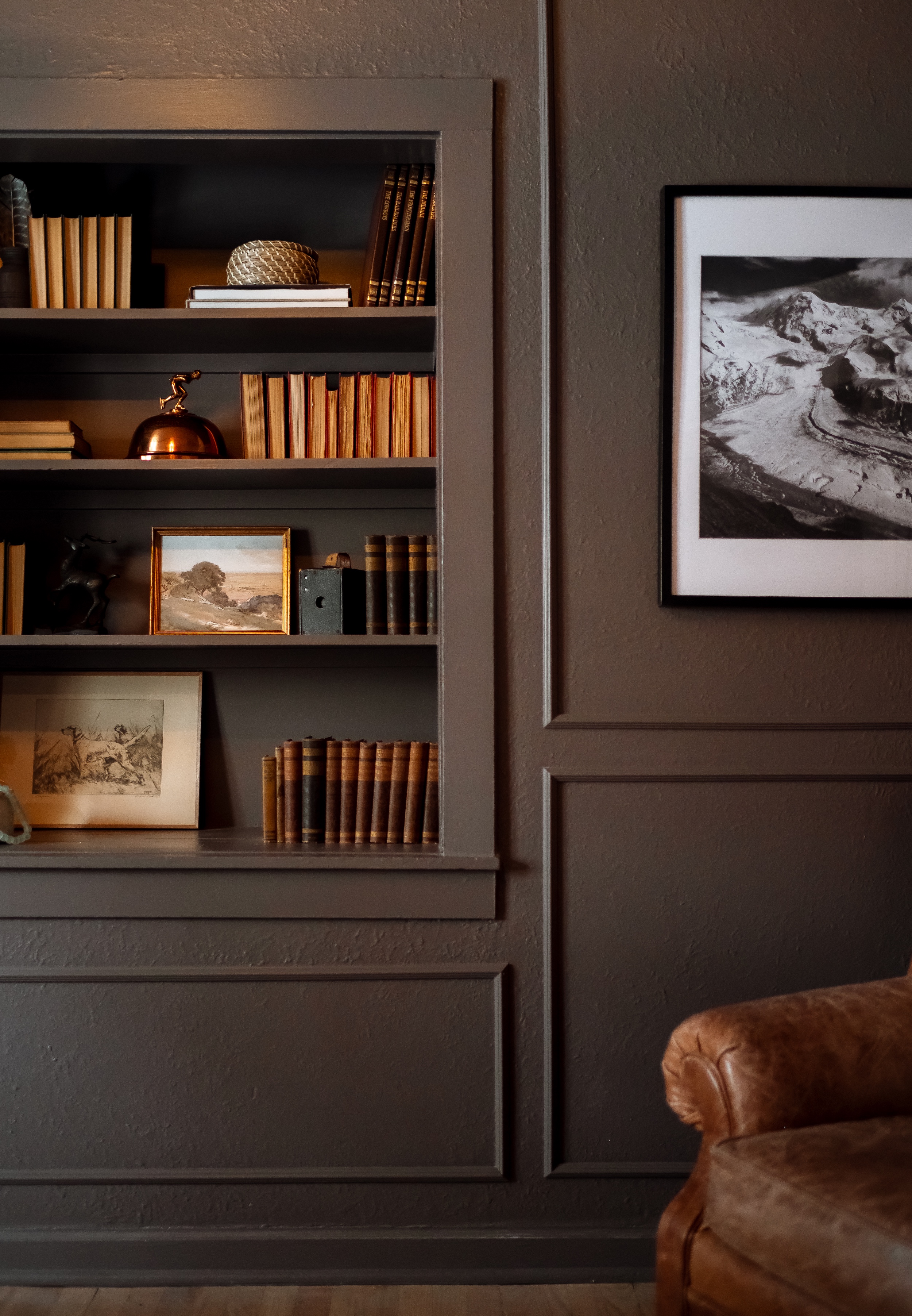 White shelving unit with decorative bottles, glasses, flower vase, framed tree print, cut lemons, and stacked books.