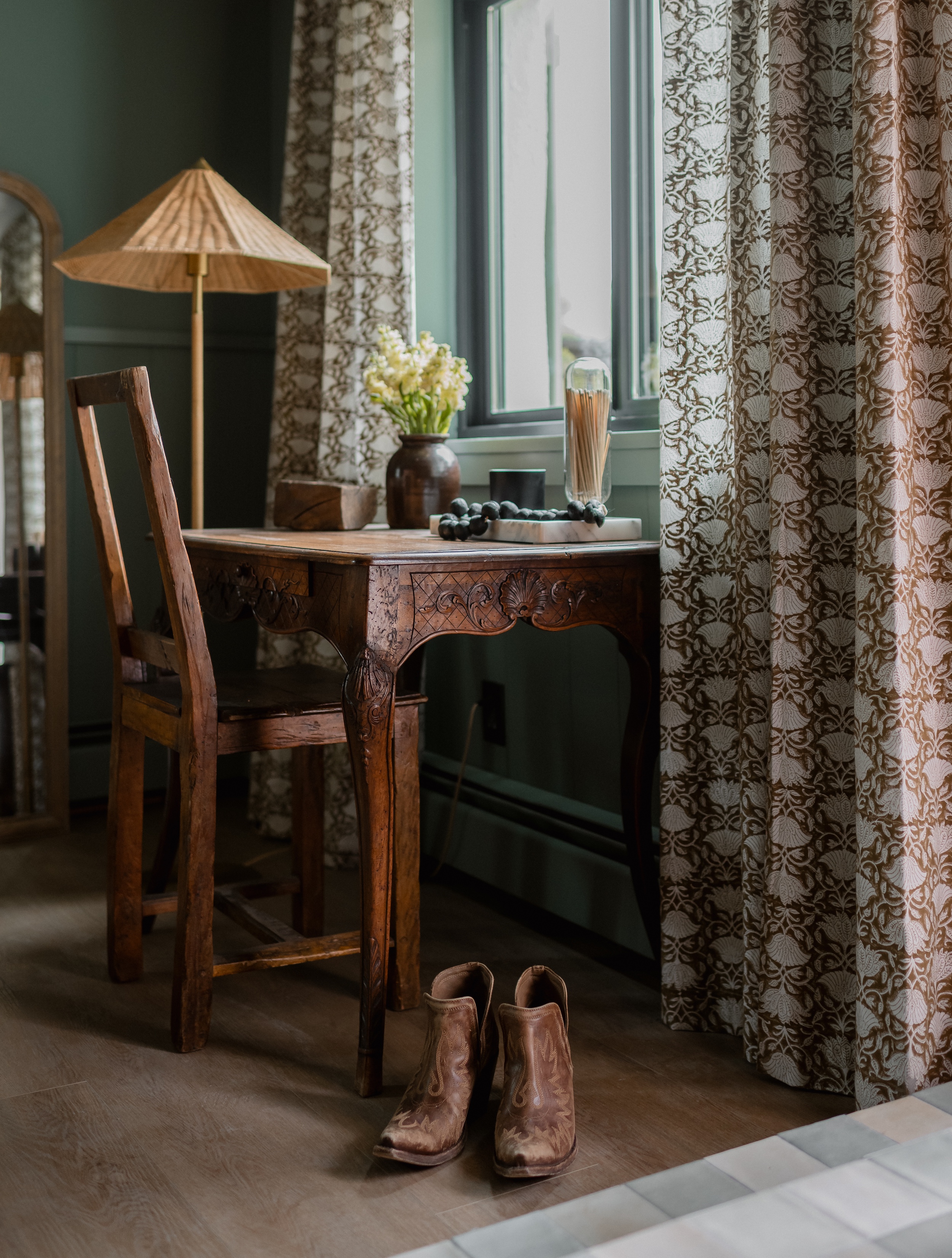 Modern kitchen sink area with brass faucet, beige cabinets, black tile backsplash, wooden shelf with dishes and decor.