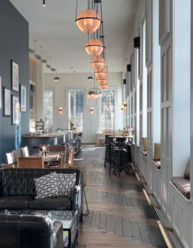 Calm lake with clear reflections of clouds and surrounding forested mountains under a blue sky.