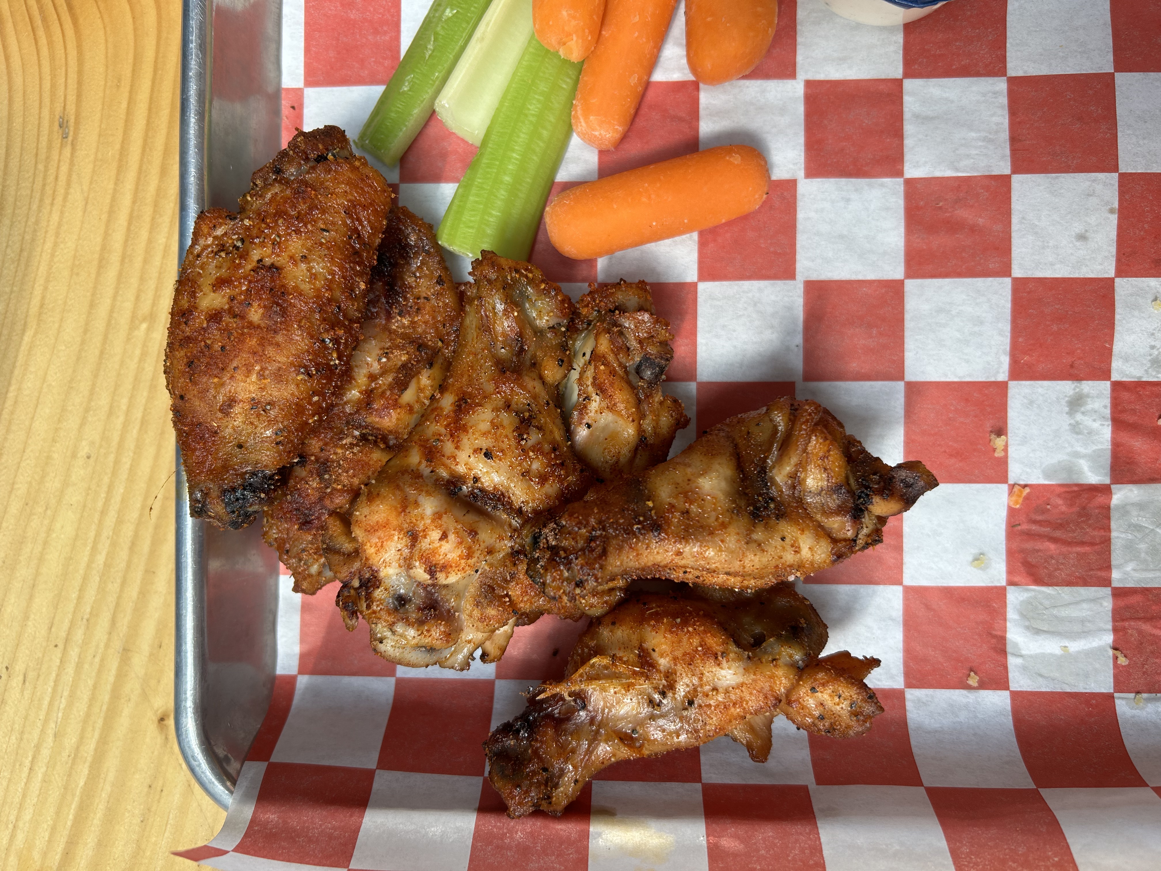Hand holding a buffalo wing with a beer and creek in the background at Busey Brews, Nederland Colorado