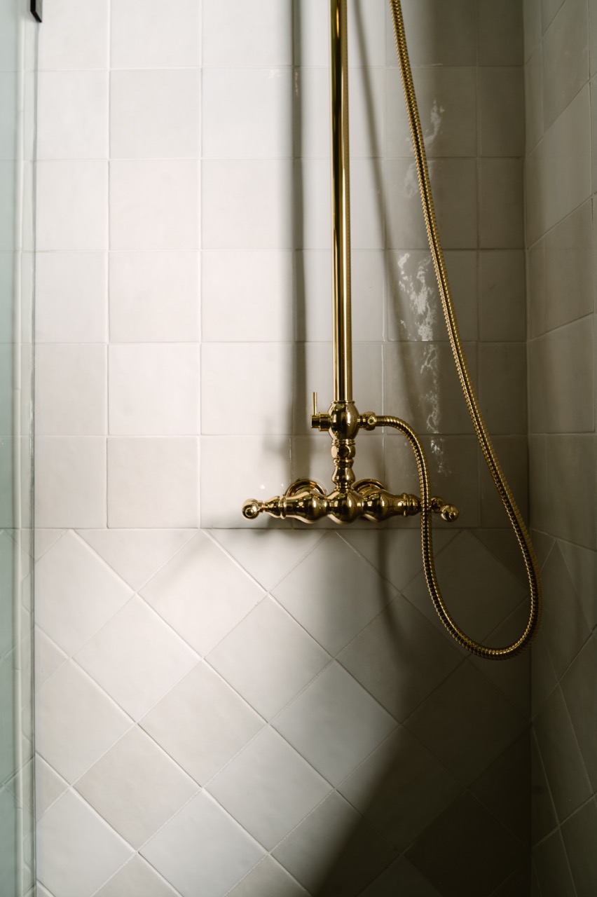 Elegant bathroom with marble countertop, brass fixtures, green flowers in a black vase, and a clawfoot bathtub with brass piping.