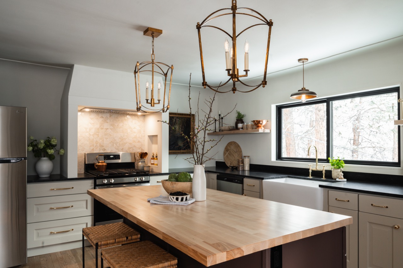 Modern kitchen with stainless steel appliances, wooden island with stools, black countertops, large window, and decorative lighting fixtures.