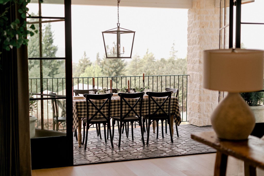 Outdoor dining area with a table covered in a black and white checkered tablecloth, six black cross-back chairs, and a hanging lantern light above.