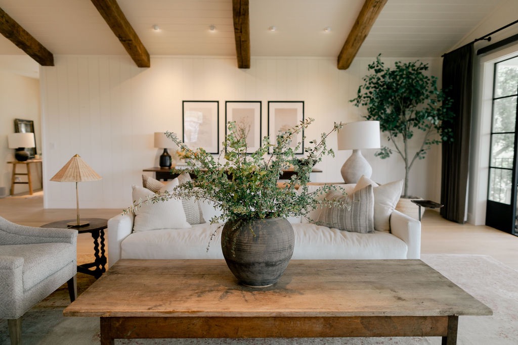 Modern kitchen with white cabinets, black tiled backsplash, brass faucet, wooden shelf holding glassware, and a stove on the right.