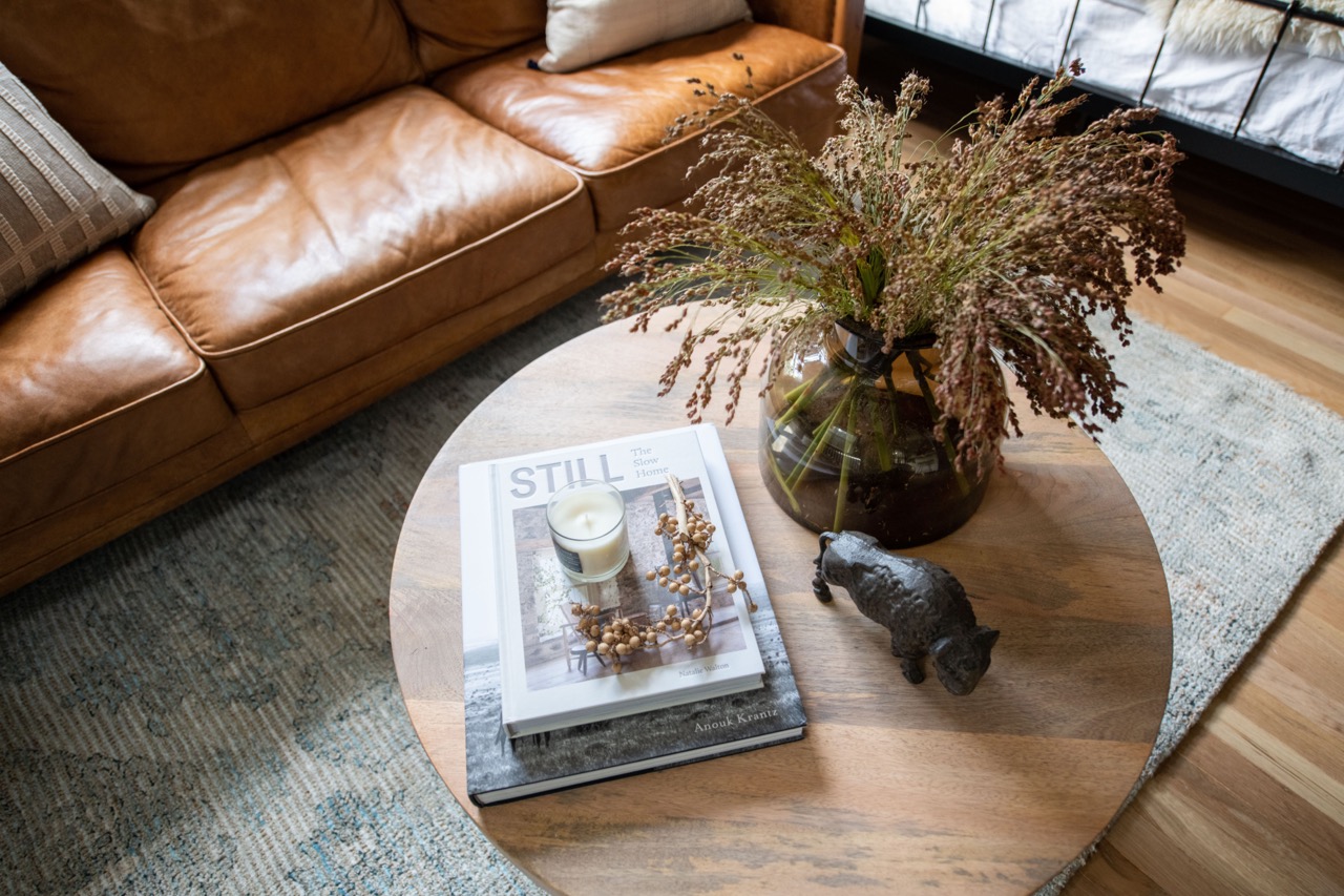 Dark wooden bookshelf filled with old books, decorative objects, a vintage clock, and a lacrosse stick, with plaid curtains to the right.