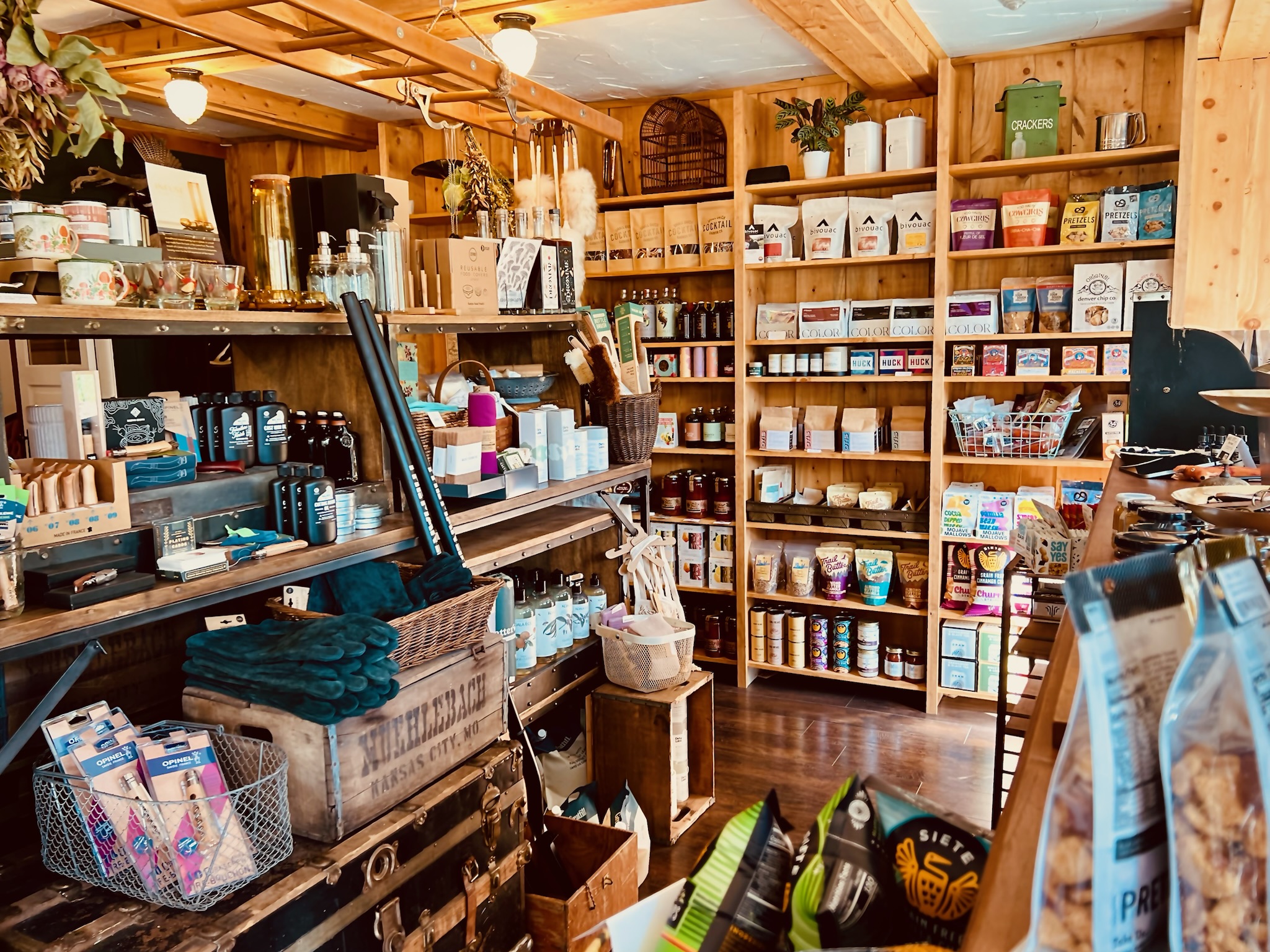 Cozy wooden shelves and counters filled with assorted packaged snacks, personal care items, and kitchenware in a rustic retail store, Blackfox Provisions, Evergreen.