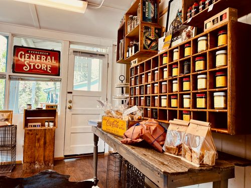 Interior of a rustic general store with wooden shelves holding jars and packaged snacks on a table at Blackfox Provisions, Evergreen.