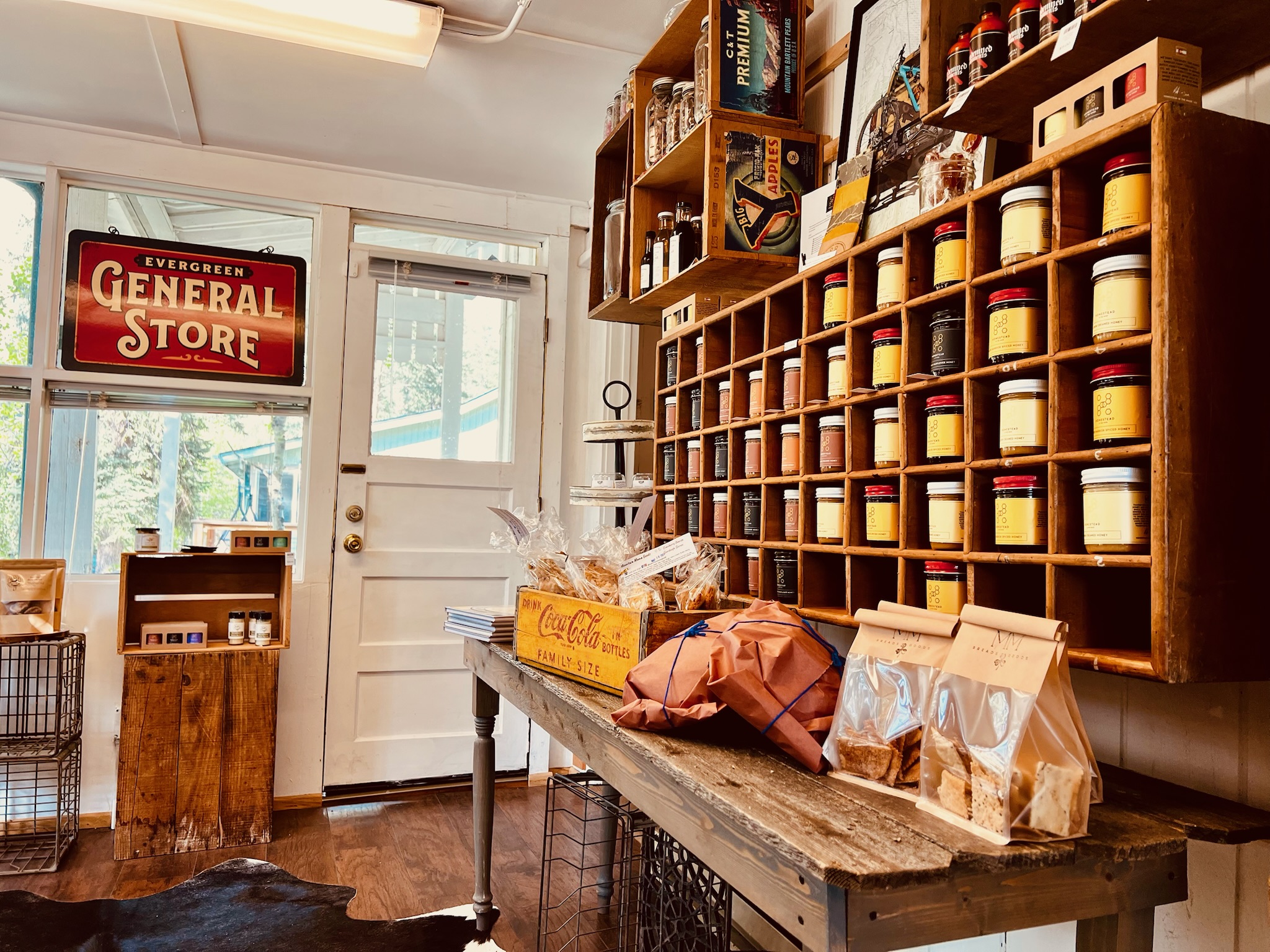 Interior of a rustic general store with wooden shelves holding jars and packaged snacks on a table at Blackfox Provisions, Evergreen.