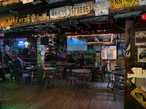 Interior of The Little Bear, a rustic bar with wooden floors, scattered tables and chairs, vintage license plates decorating the ceiling, and a few patrons seated.