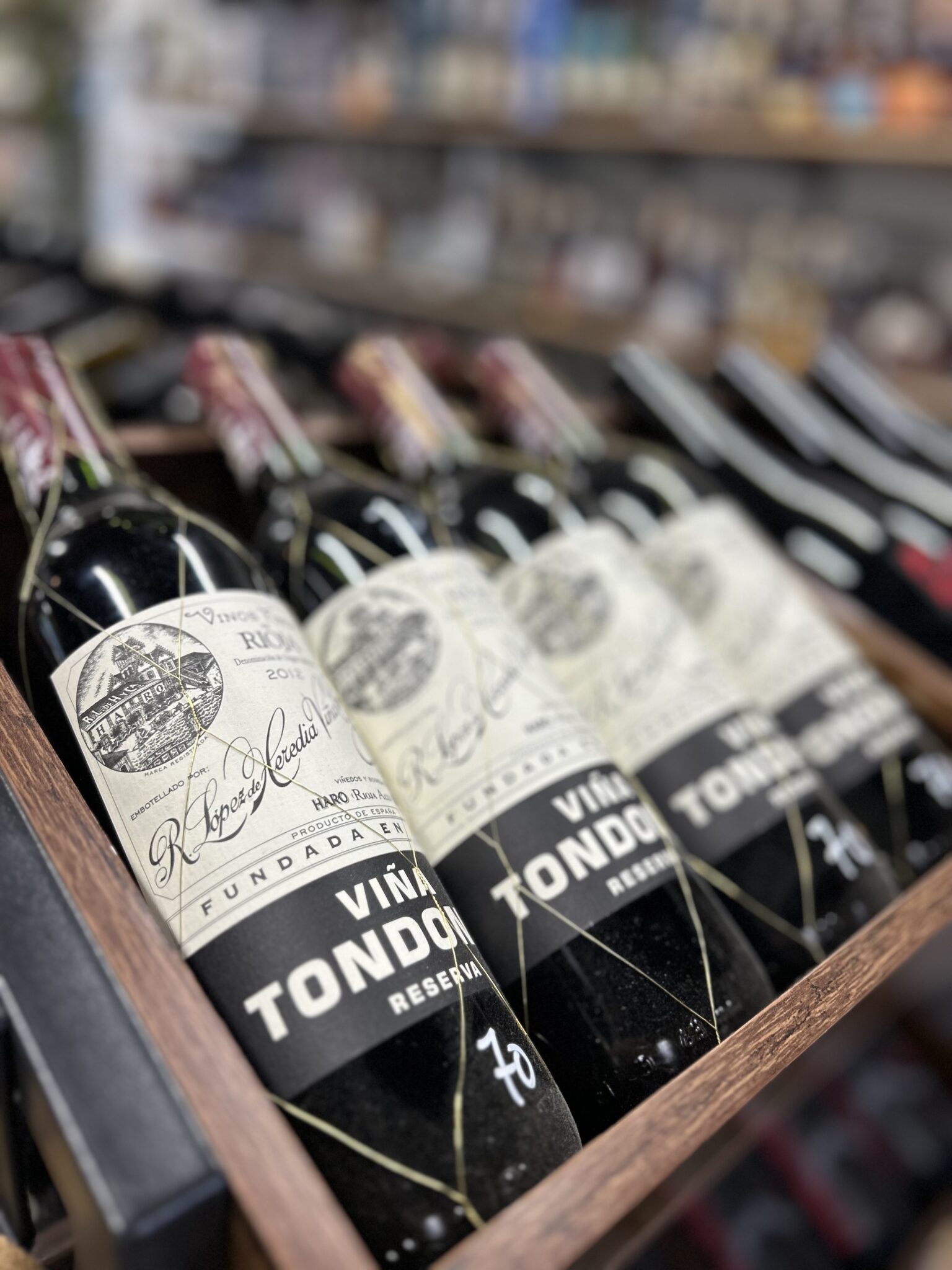 Row of Viña Tondonia Reserva red wine bottles with black and white labels in a wooden crate at Piney Wine and Spirits.