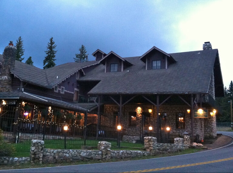 Large rustic stone and wood lodge with outdoor string lights and illuminated lamps at dusk.