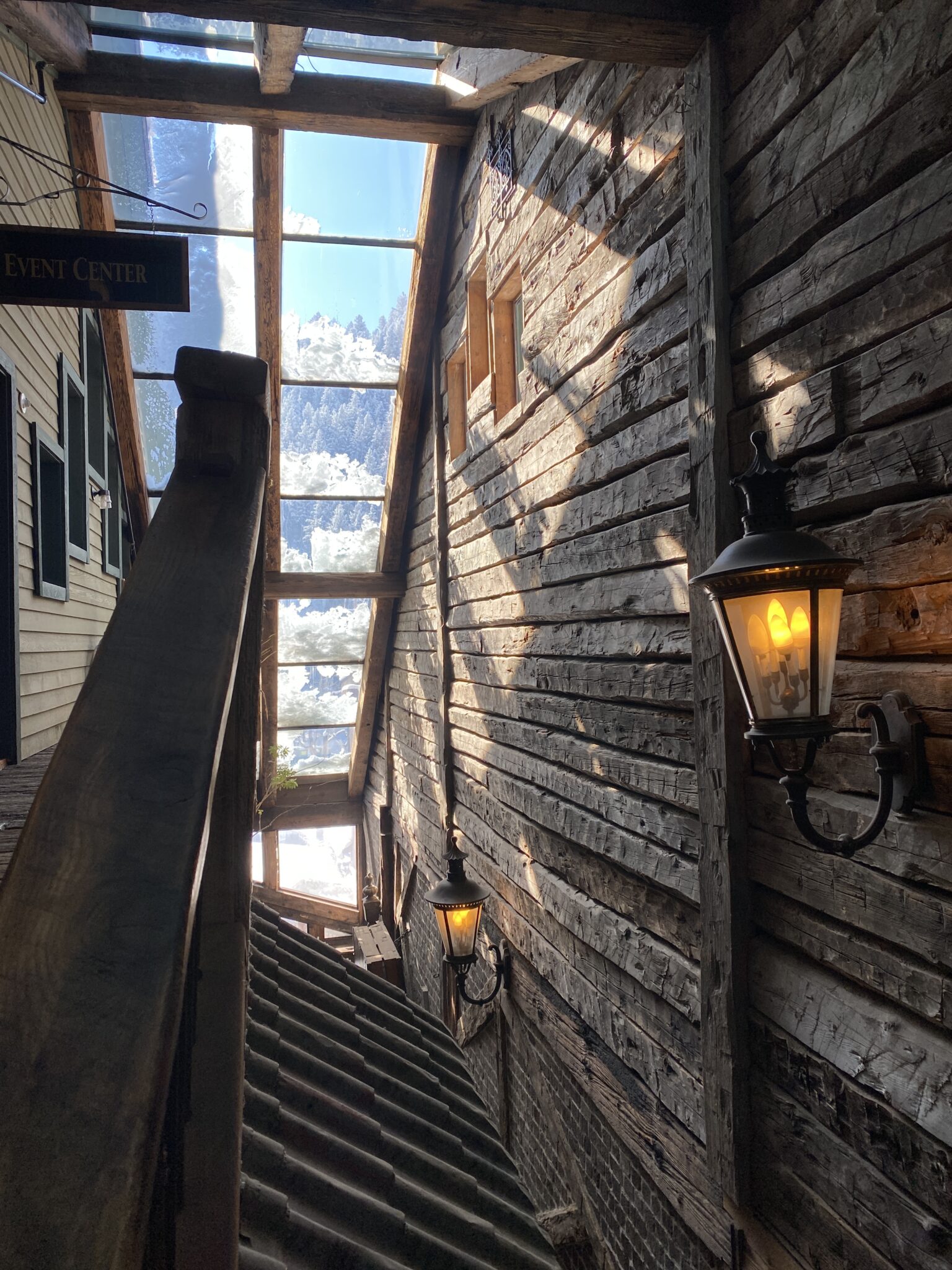 Interior corridor with rustic wooden walls, lit lanterns, and large window panels showing a snowy mountain landscape inside The Little Bear in Evergreen, Colorado.