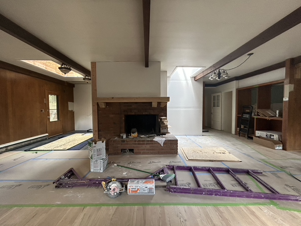 Interior of a room under renovation with a brick fireplace, construction tools, and materials on protected floor.