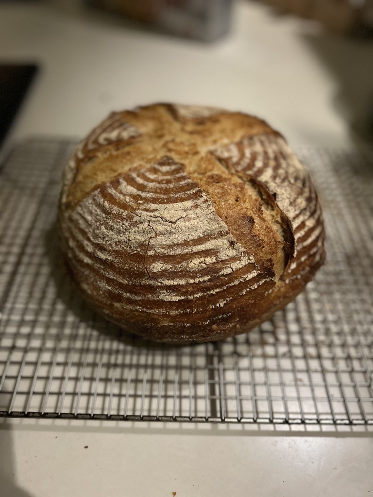 Round artisanal loaf of bread with a cross pattern on top cooling on a wire rack.