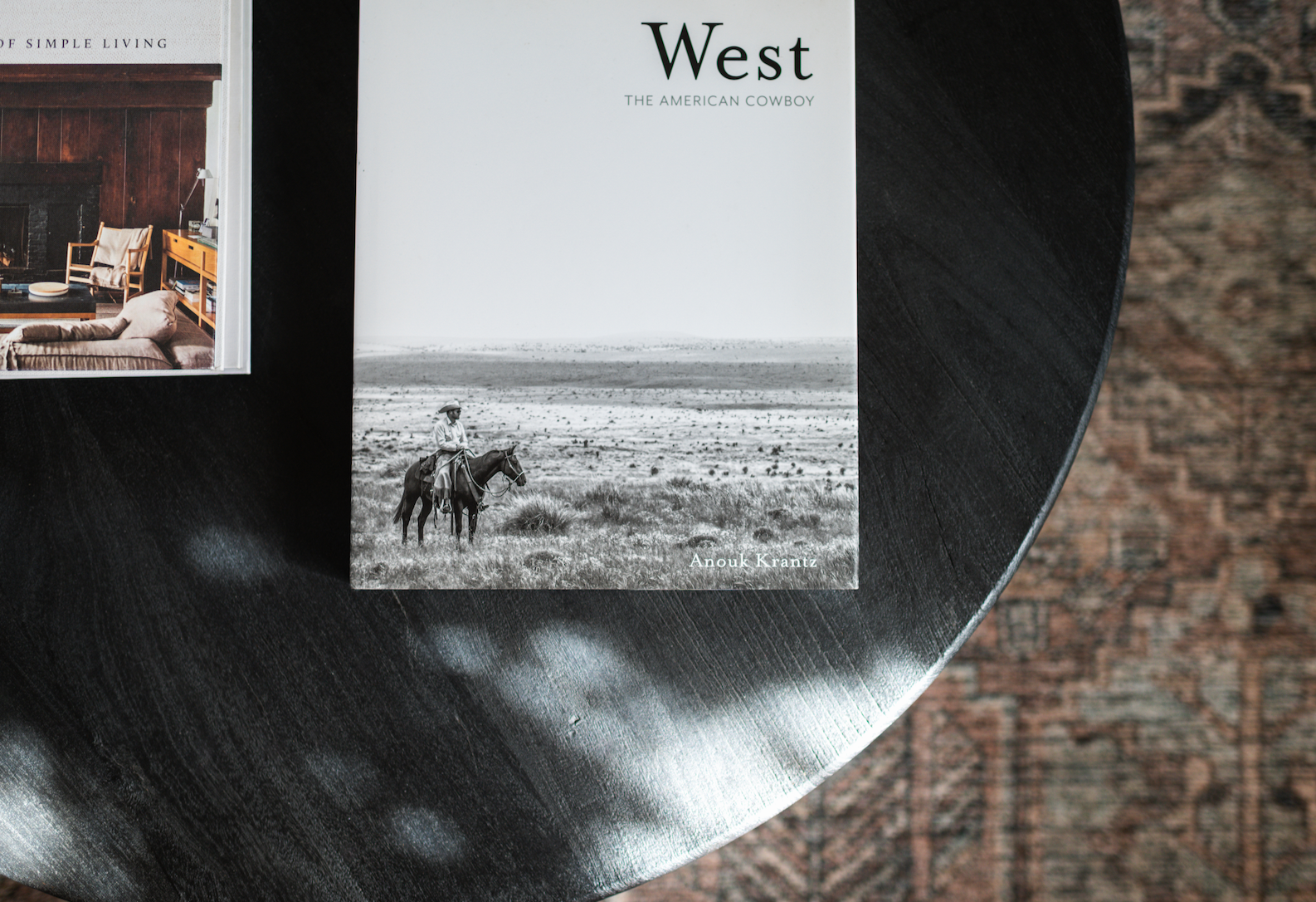 Cover of a book titled 'West The American Cowboy' showing a black and white photo of a cowboy on horseback in an open landscape.