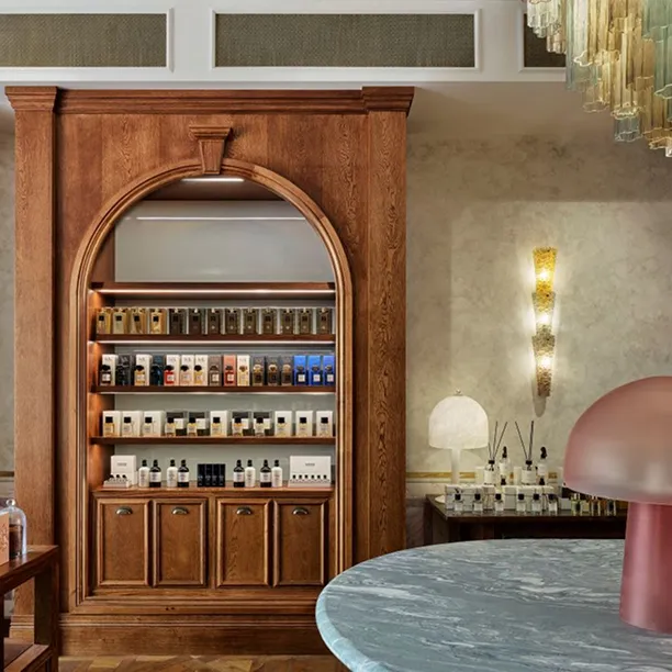 Elegant wooden display cabinet filled with various perfume bottles inside a stylish boutique with modern lighting and marble table.