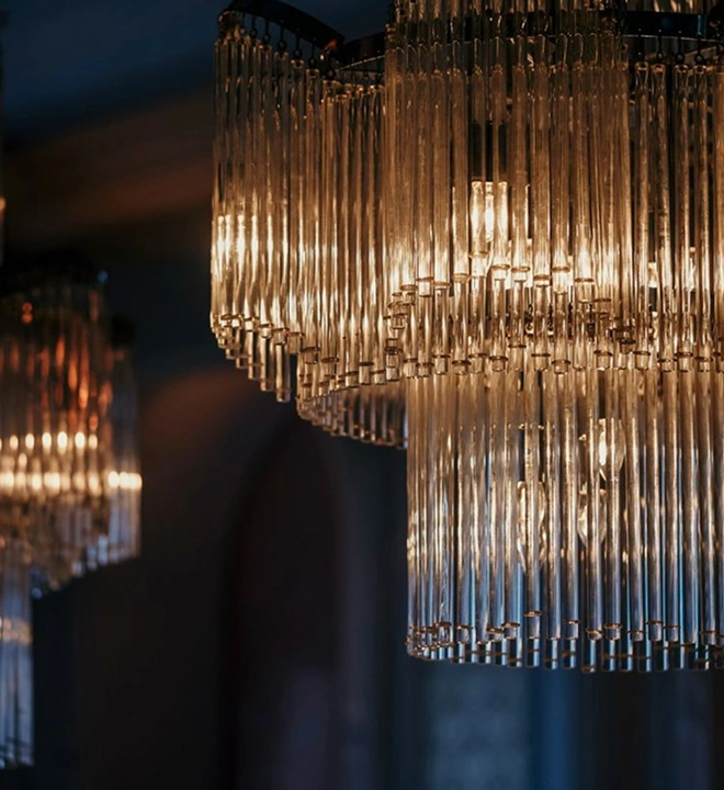 Close-up of elegant glass tube chandeliers with warm light in a dimly lit room.