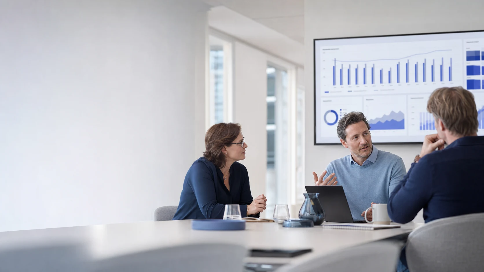 Finance Team diskutiert vor einem digitalen Dashboard in einem hellen Büro