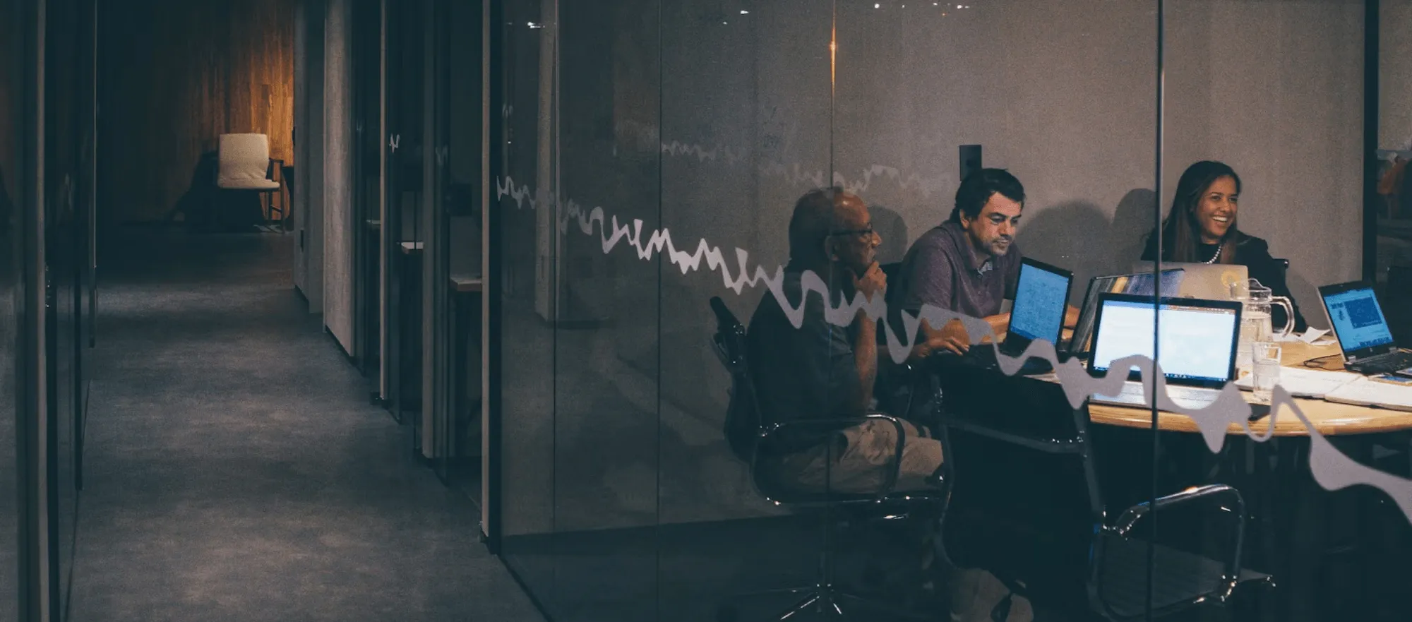 Colleagues working on laptops in a glass meeting room in the evening