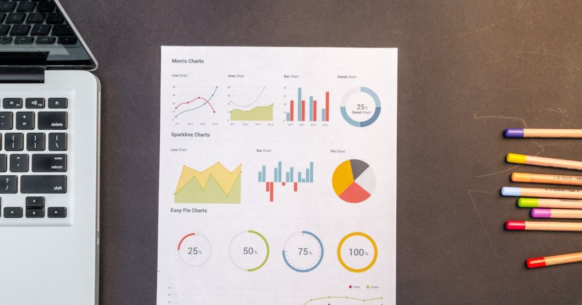 Image of a desk with a laptop, infographic with charts, and colored pencils.
