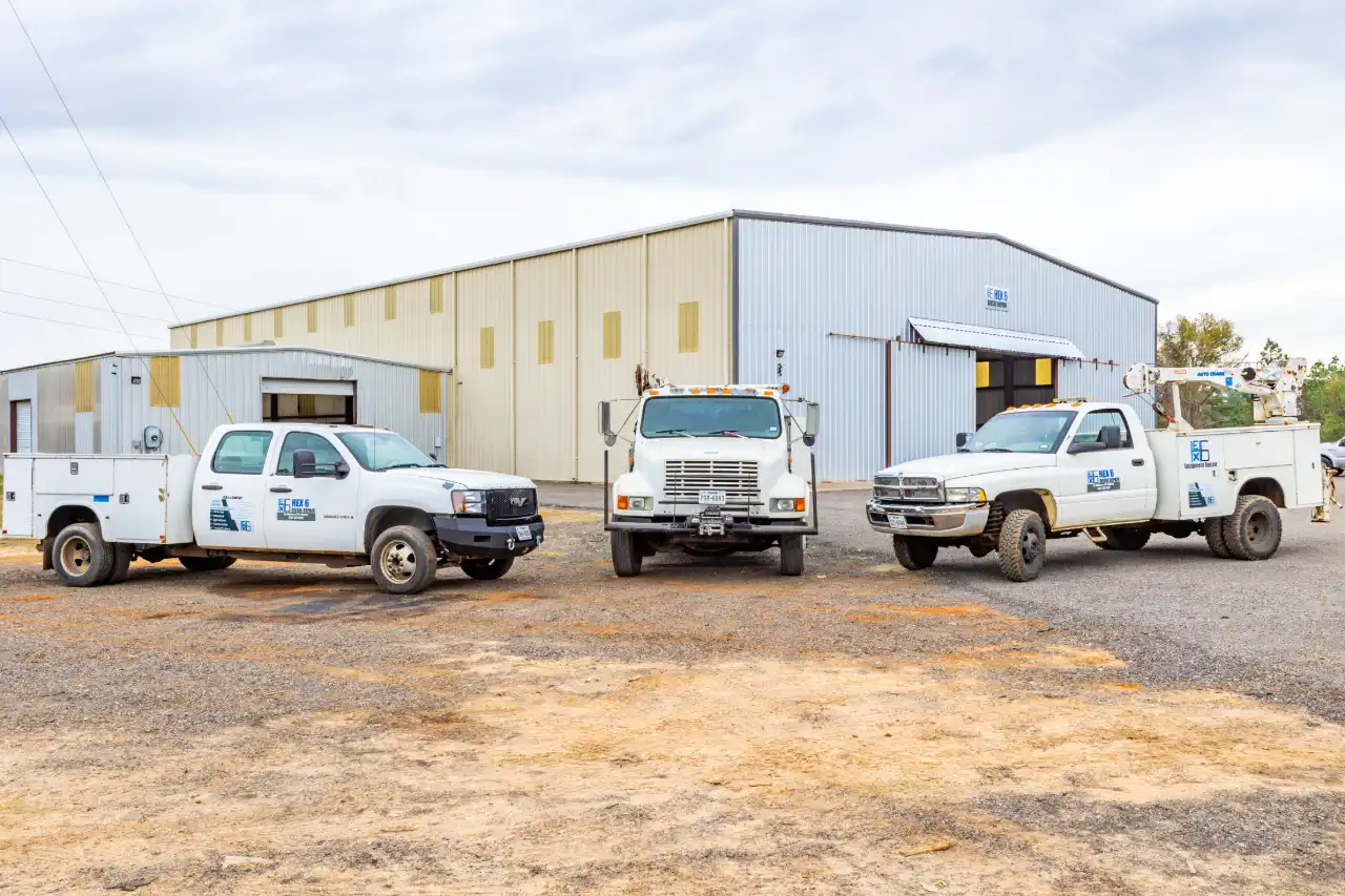 Fleet maintenance trucks bearing HEX6 logo lined up outside metal workshop, boom-equipped pickup ready for site repairs.