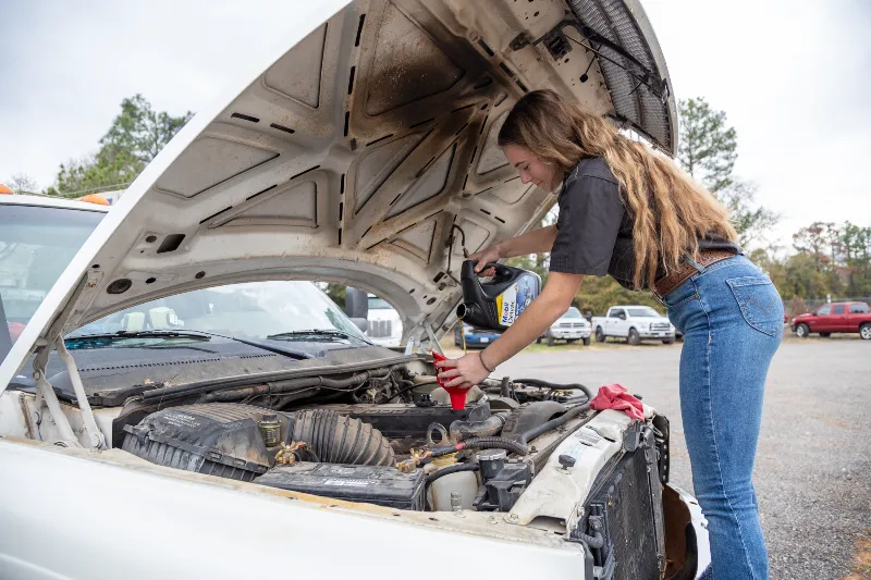 Oil change service as tech pours Mobil oil into pickup engine with hood raised and red funnel.
