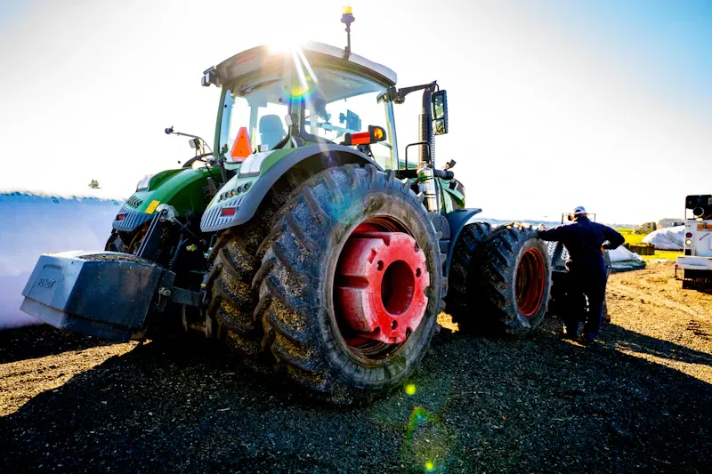 Tractor repair technician servicing a large agricultural tractor with dual rear tires removed for maintenance.