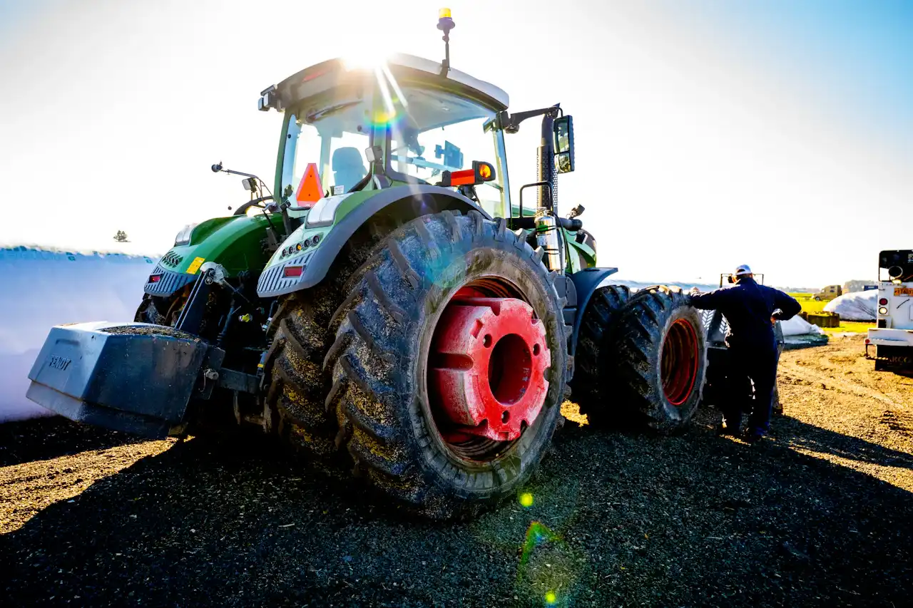 Tractor repair technician servicing a large agricultural tractor with dual rear tires removed for maintenance.
