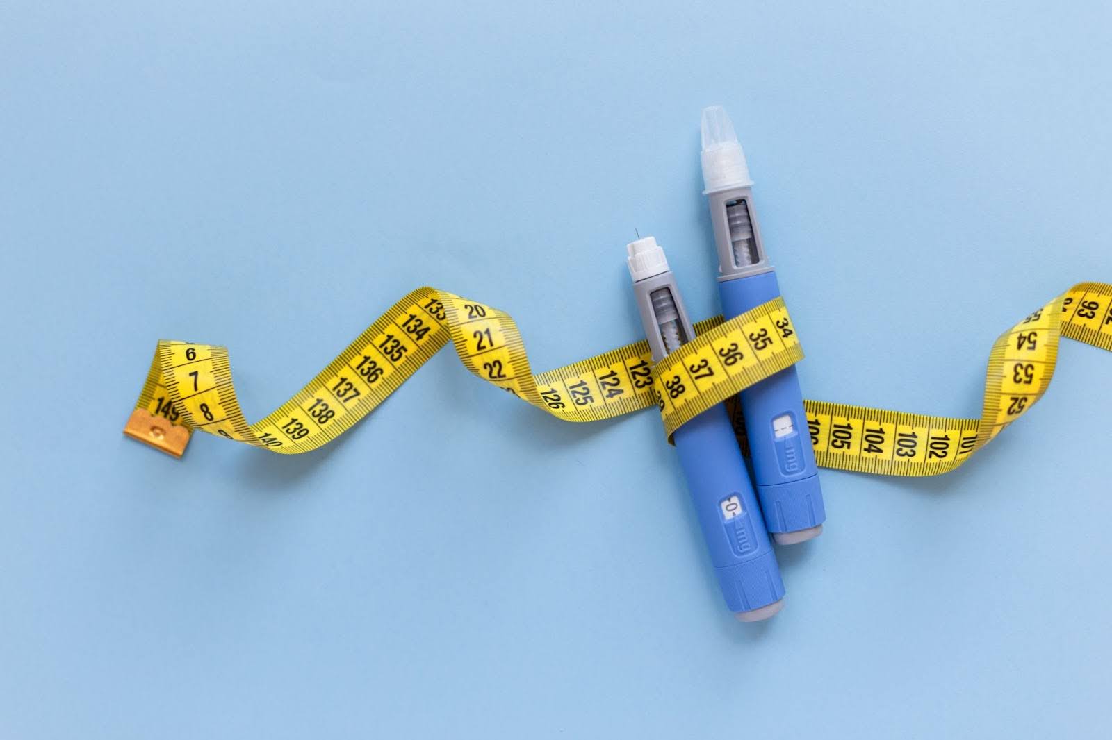 Two semaglutide injection pens for weight loss wrapped with a yellow measuring tape.