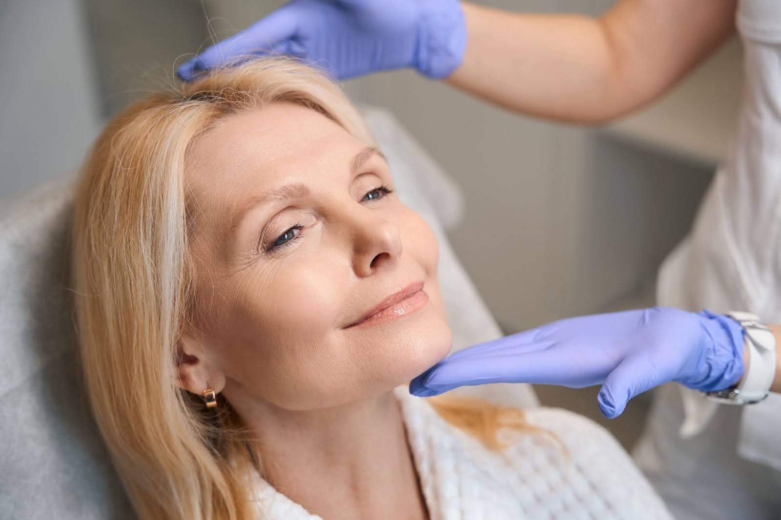 Gloved hands frame a woman's face with glowing skin, highlighting the results of a professional skincare treatment.