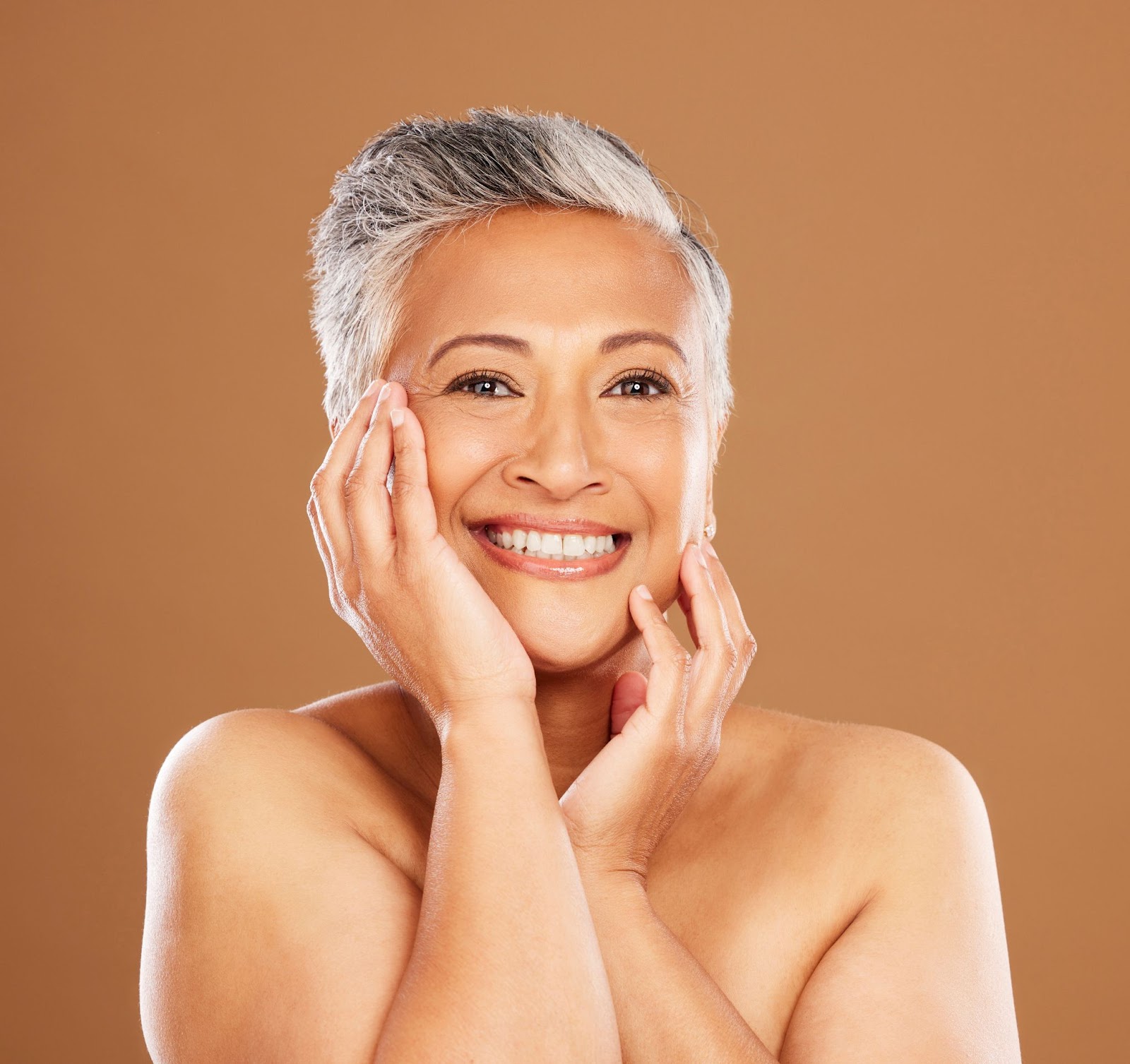 A proud senior woman touches her radiant skin, showcasing visible improvement after regular collagen peptide use.
