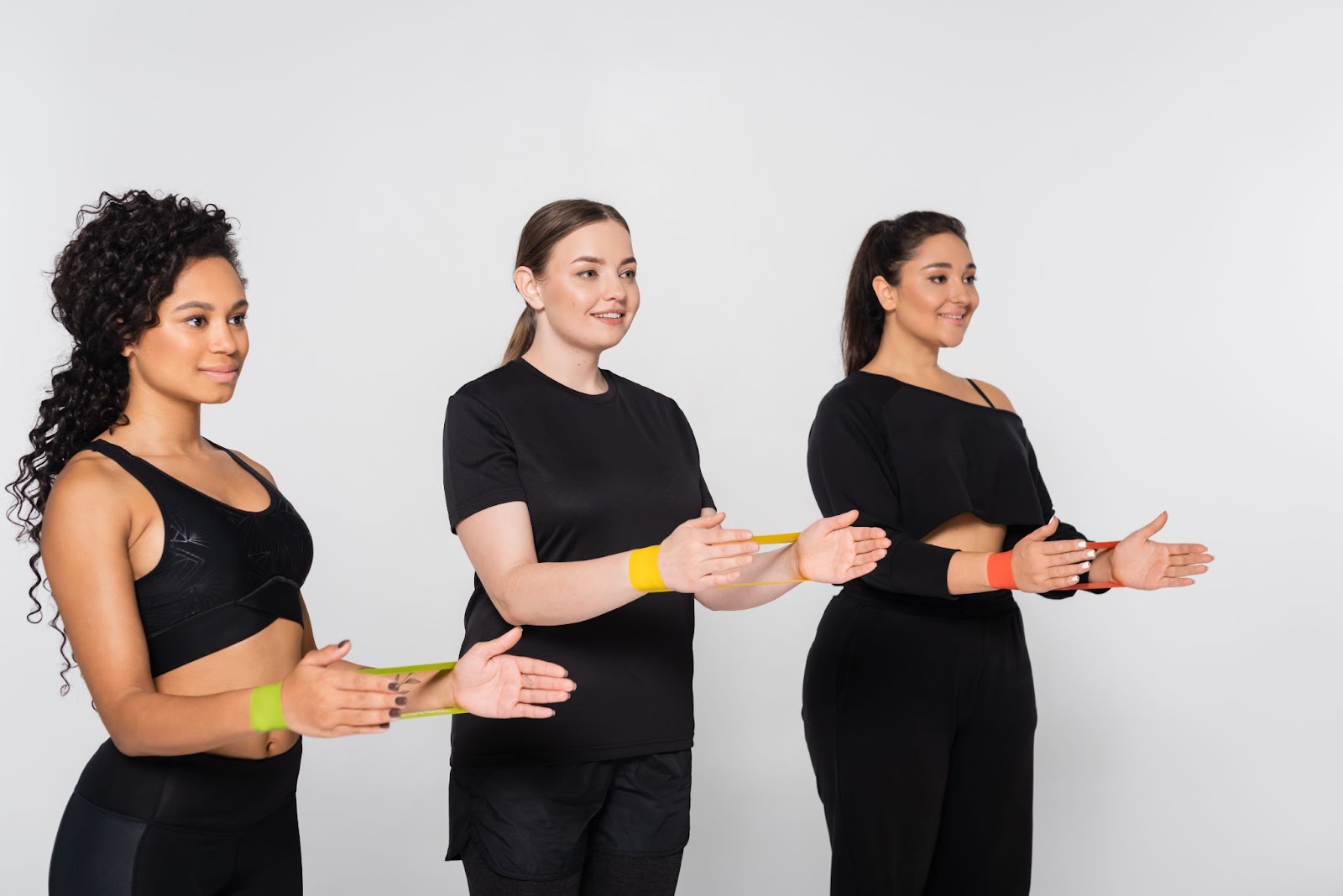 Three women performing resistance band exercises during a fitness training session.
