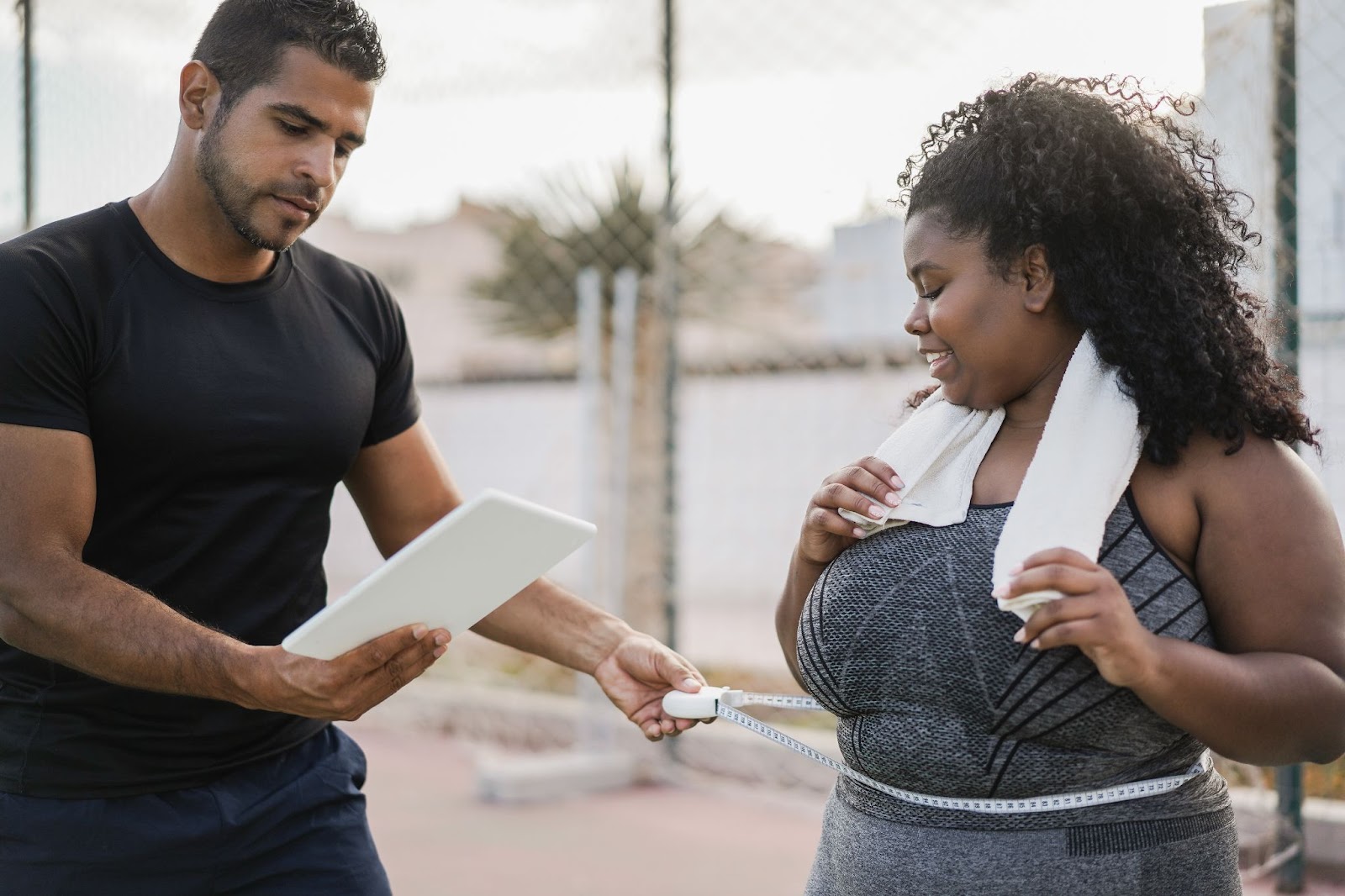 A curvy woman with her trainer measuring her waist as part of a fitness assessment.