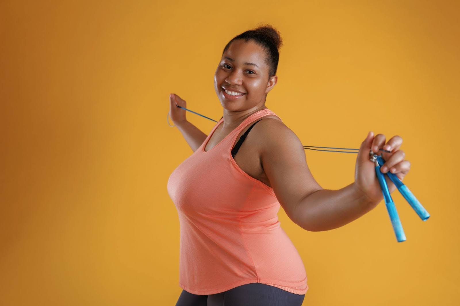 African American woman standing confidently with a jump rope draped around her shoulders against a bright yellow background.