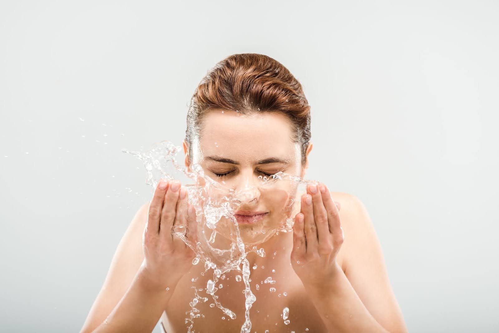 Woman with closed eyes gently washing her face.
