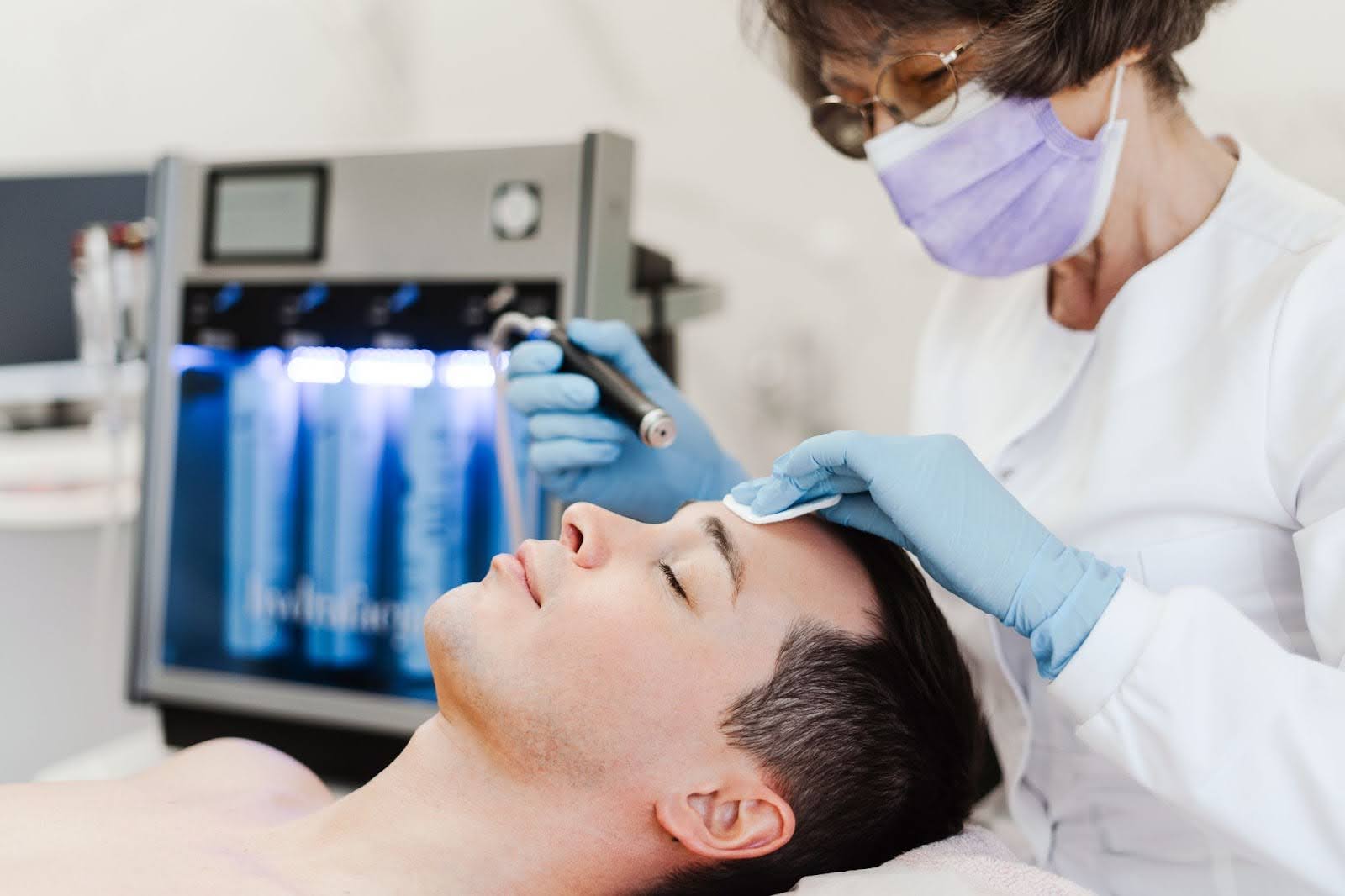 A male is getting a facial done by a lady esthetician.