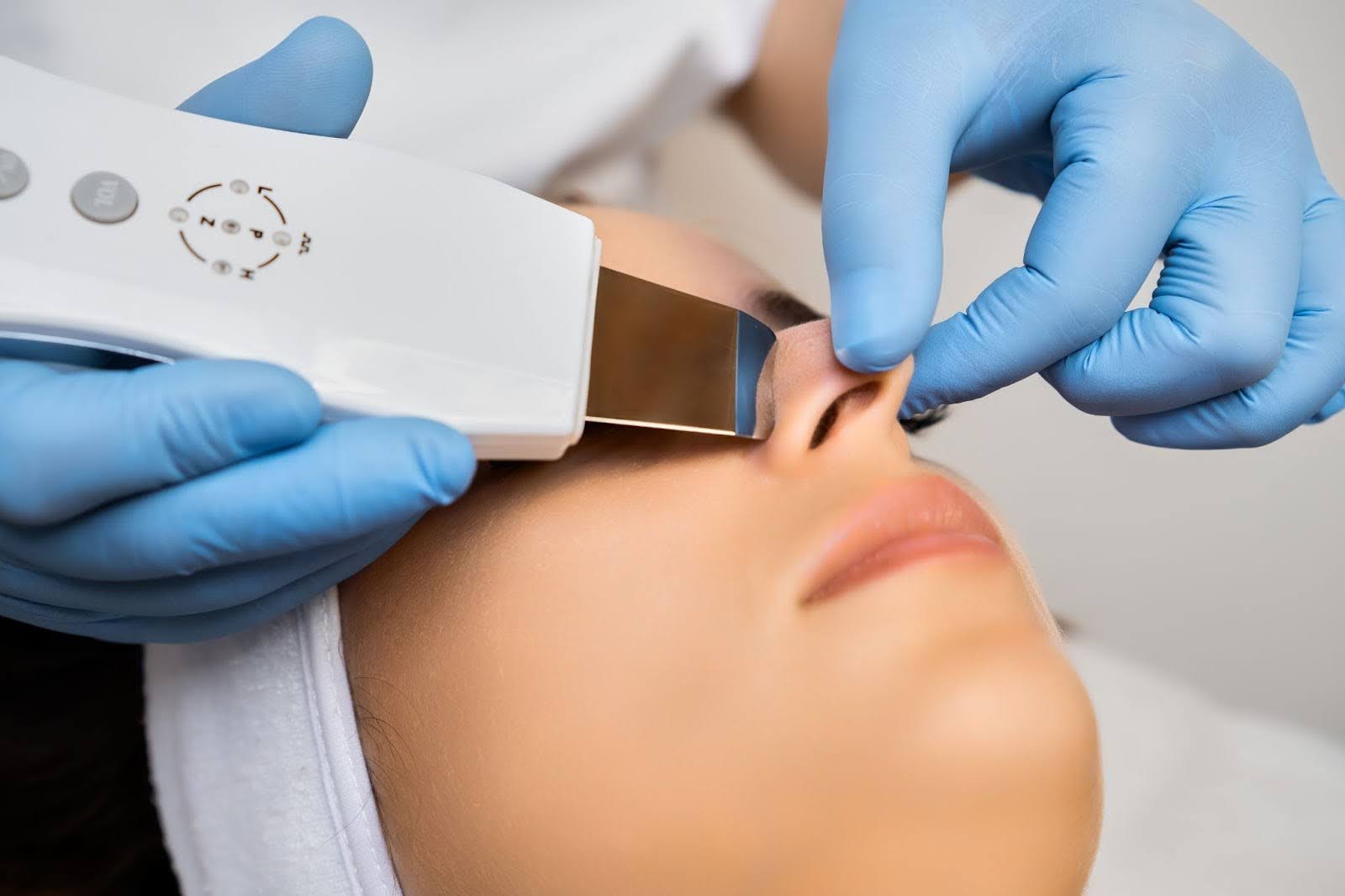 A cosmetologist dermaplanes a woman’s nose with special equipment.