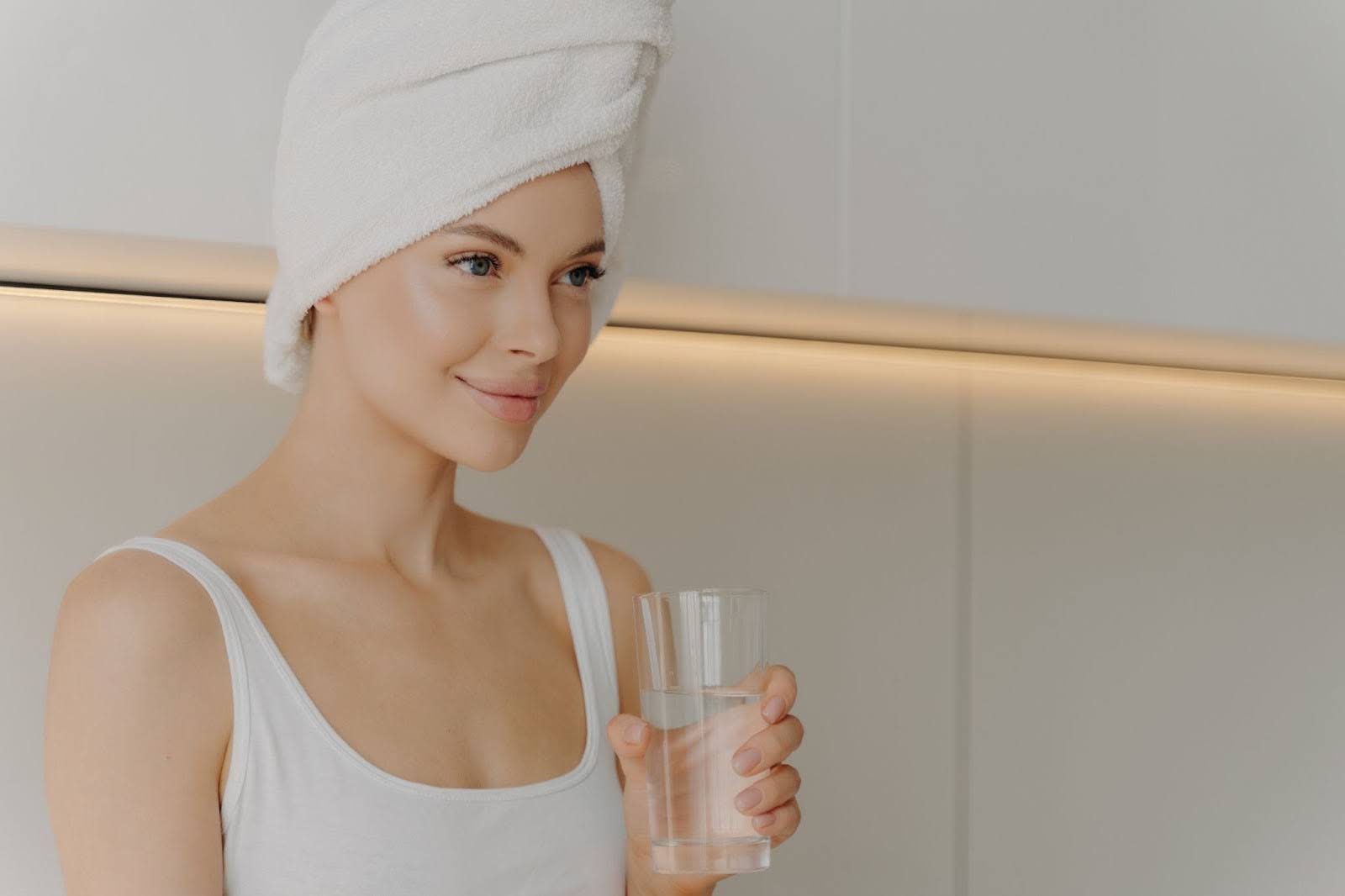 Smiling woman with radiant, healthy skin enjoying a glass of clear water.