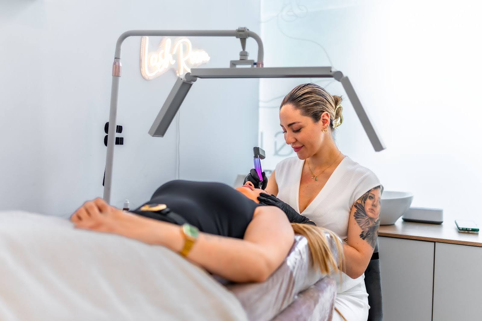 Tattooed esthetician performing laser tattoo removal on a client’s shoulder.