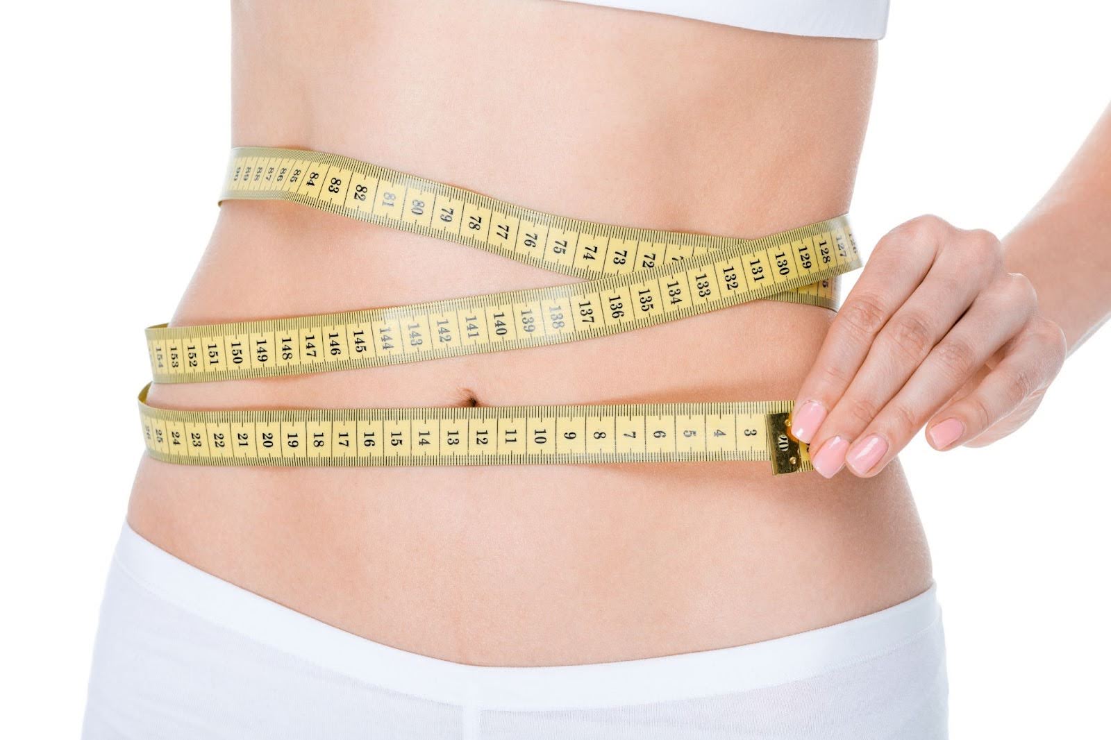 Partial view of a young woman checking her waist size with a measuring tape.