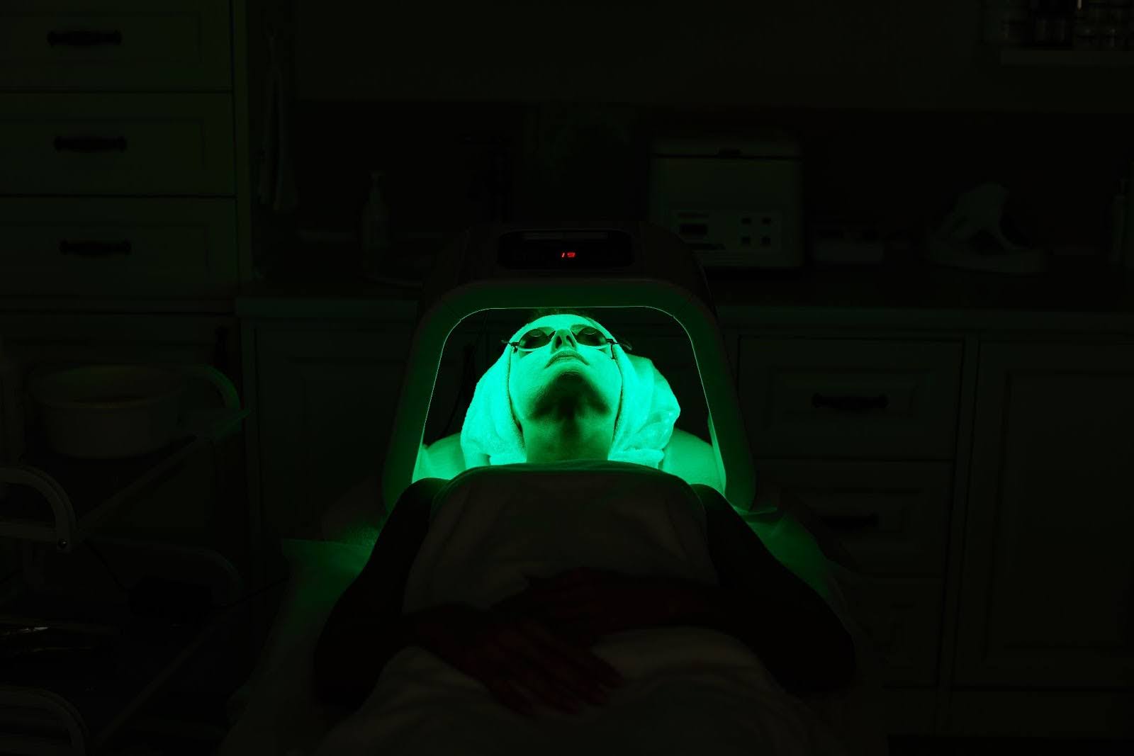 Woman receiving a facial treatment with LED light therapy in a dimly lit room.