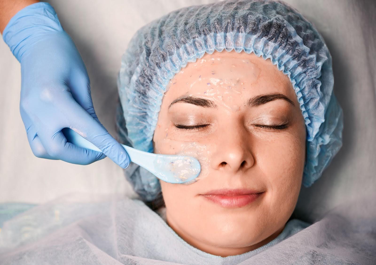 Facial treatment showing an esthetician applying a pore-refining mask to improve skin texture.