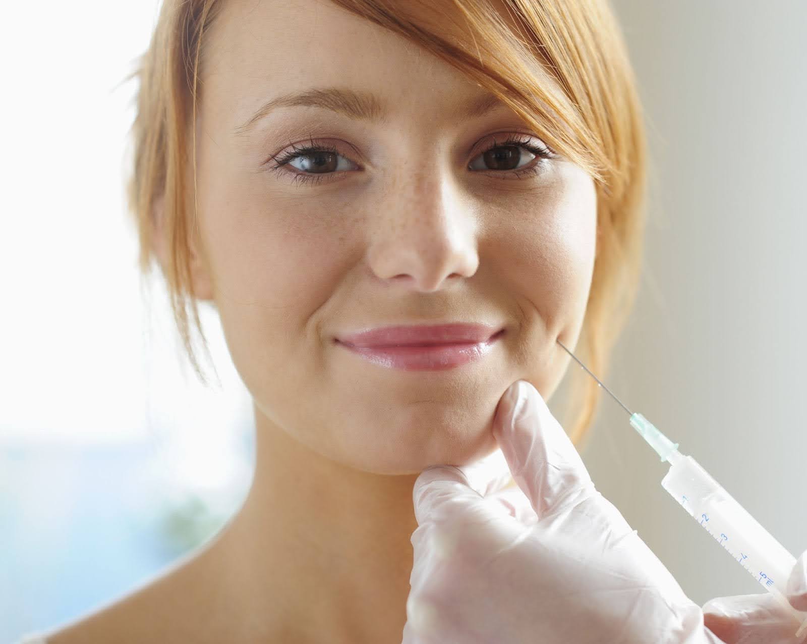 Young redheaded woman receiving injectable treatment to enhance cheek volume.
